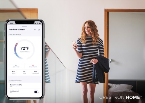 Woman using smartphone to adjust home climate control system. Closeup of Crestron app interface in foreground.