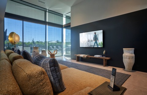 Crestron remote control on a side table in a comfortable living room. A TV and large windows are in the background