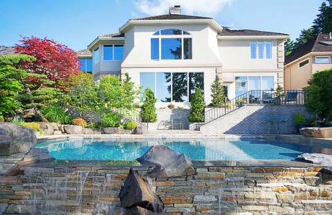 outdoor view of a backyard with a pool and luxury home in the background.