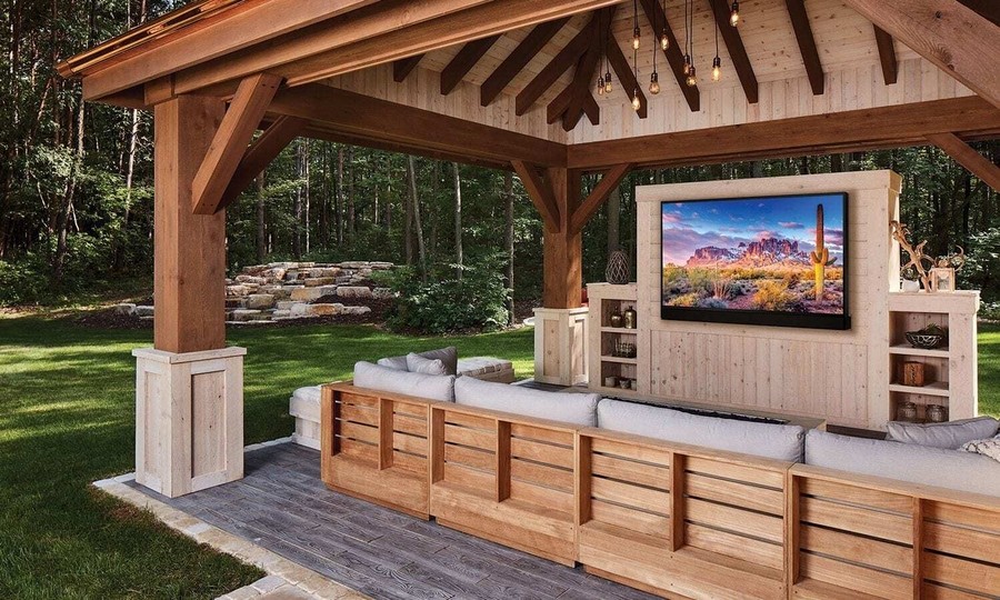 outdoor luxury patio with a wall-mounted Séura outdoor TV in front of a seating area under a patio cover.