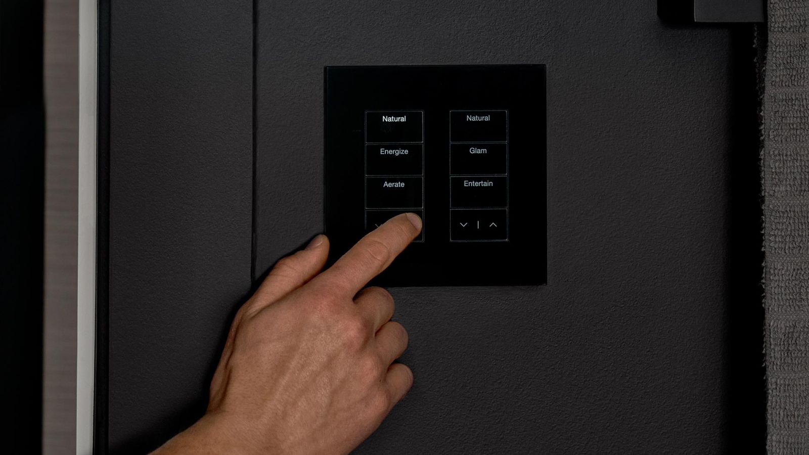 Person using a black touch panel with labeled lighting scene buttons